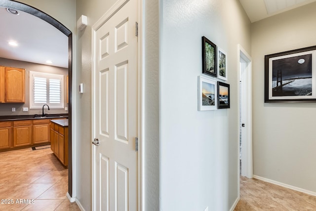 corridor featuring a sink, baseboards, and light tile patterned flooring