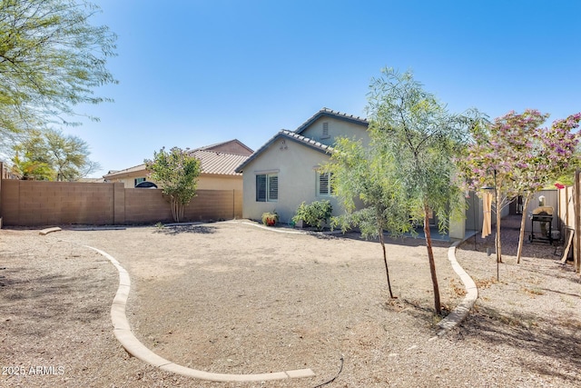 rear view of property with a tiled roof, stucco siding, and fence private yard