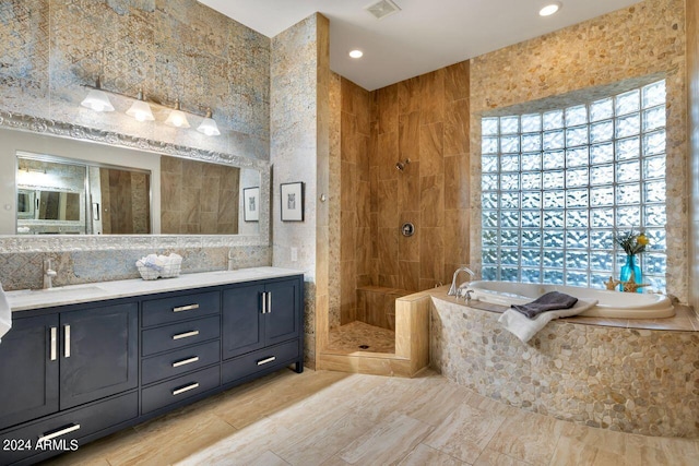 bathroom featuring plus walk in shower, vanity, and tile walls