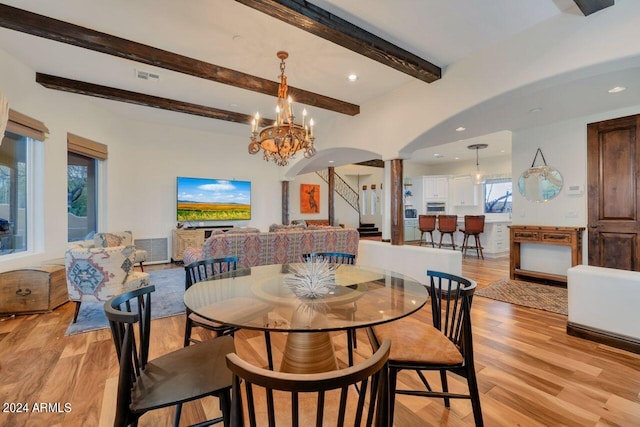 dining space with decorative columns, a notable chandelier, beam ceiling, and light hardwood / wood-style flooring