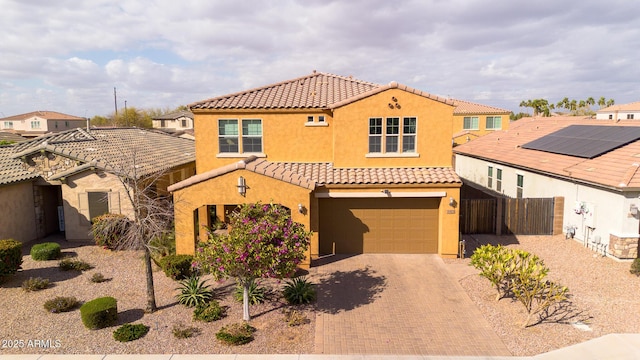 mediterranean / spanish-style home with fence, a tile roof, stucco siding, decorative driveway, and an attached garage