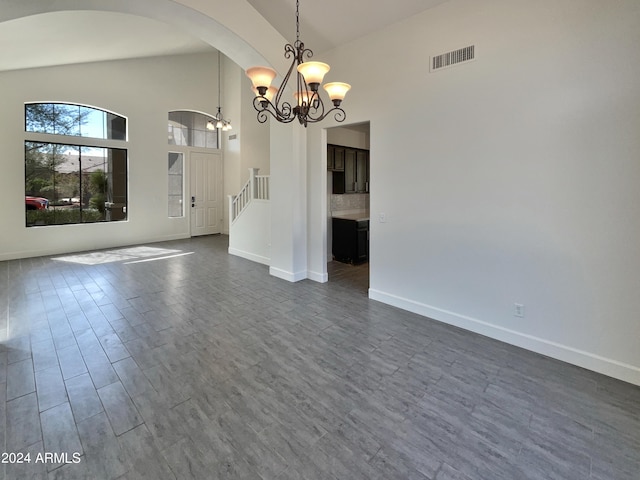 unfurnished dining area featuring an inviting chandelier, dark hardwood / wood-style floors, and high vaulted ceiling