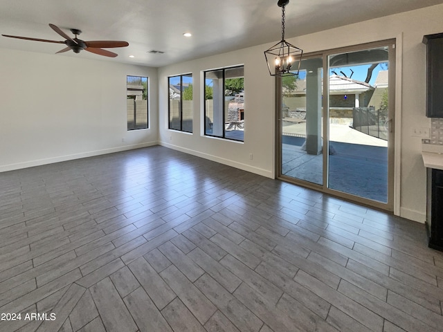 spare room with ceiling fan with notable chandelier and wood-type flooring