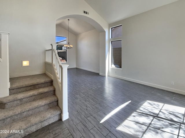 stairway with hardwood / wood-style floors, high vaulted ceiling, and a notable chandelier