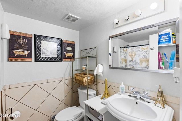 bathroom featuring toilet, a textured ceiling, tile walls, and sink