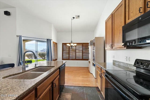 kitchen with sink, an inviting chandelier, pendant lighting, dark stone counters, and black appliances