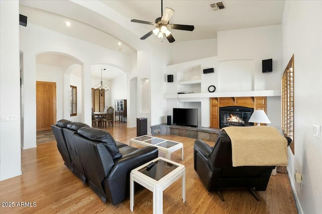 living room with a tile fireplace, ceiling fan with notable chandelier, high vaulted ceiling, light hardwood / wood-style flooring, and built in shelves