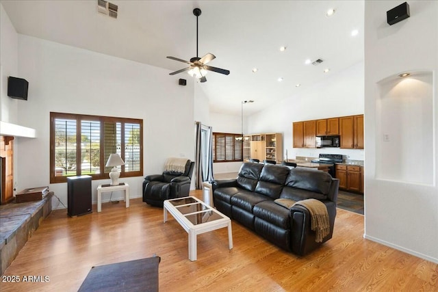 living room with a towering ceiling, ceiling fan, and light wood-type flooring