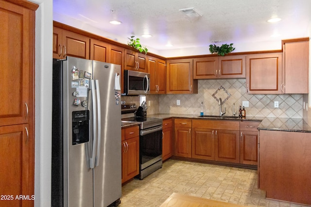 kitchen with visible vents, decorative backsplash, appliances with stainless steel finishes, brown cabinetry, and a sink