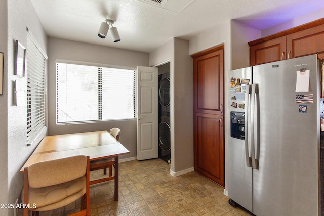 kitchen with brown cabinets, stainless steel refrigerator with ice dispenser, stone finish flooring, a textured ceiling, and baseboards