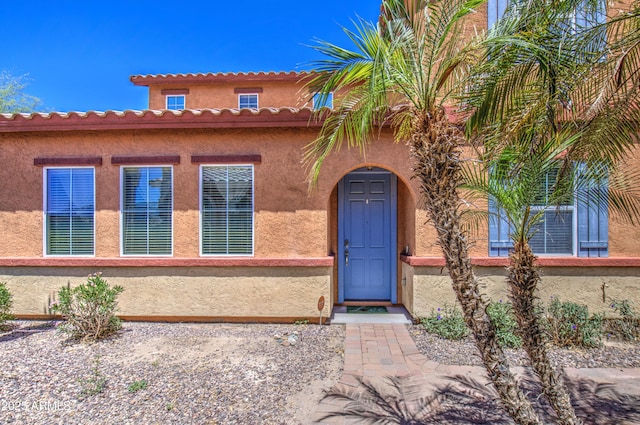 view of exterior entry with stucco siding and a tile roof