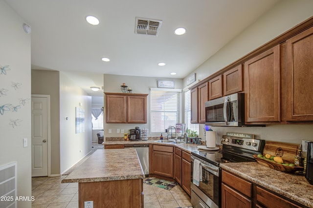 kitchen with appliances with stainless steel finishes, a sink, light tile patterned floors, a kitchen island, and brown cabinetry