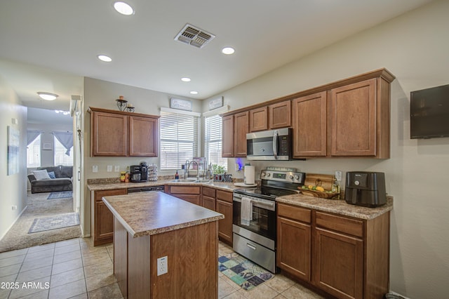 kitchen with appliances with stainless steel finishes, a center island, a sink, light tile patterned flooring, and brown cabinets