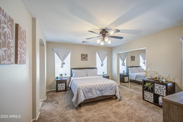 carpeted bedroom with multiple windows, arched walkways, ceiling fan, and a closet
