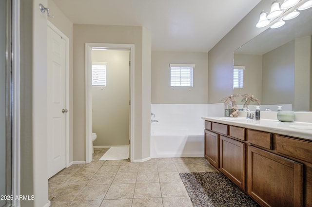full bathroom featuring toilet, a bath, vanity, tile patterned floors, and baseboards