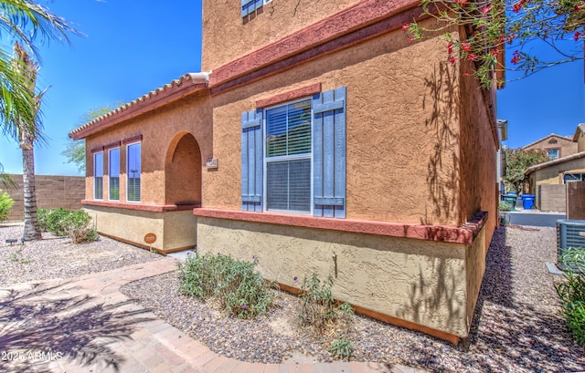 view of home's exterior with fence, stucco siding, and central AC