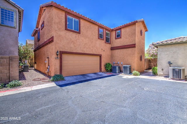 back of property featuring an attached garage, central air condition unit, and stucco siding