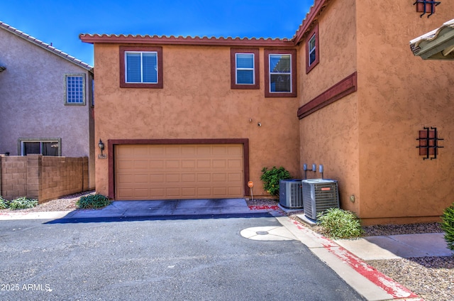 view of front of house with central air condition unit, a garage, asphalt driveway, fence, and stucco siding