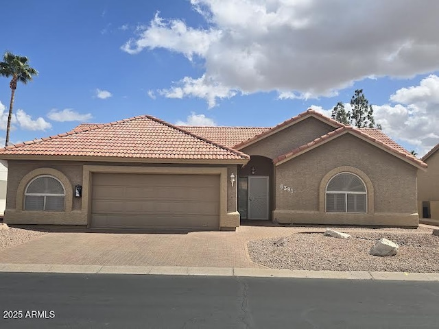 mediterranean / spanish home featuring stucco siding, an attached garage, a tile roof, and decorative driveway