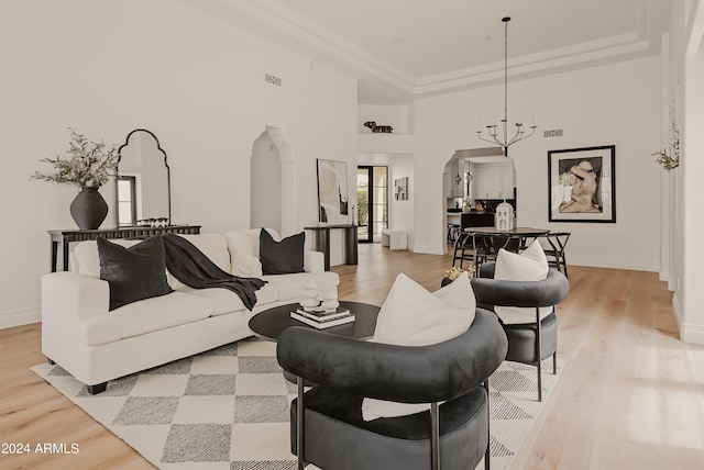 living room featuring a high ceiling, light hardwood / wood-style flooring, a raised ceiling, and a chandelier