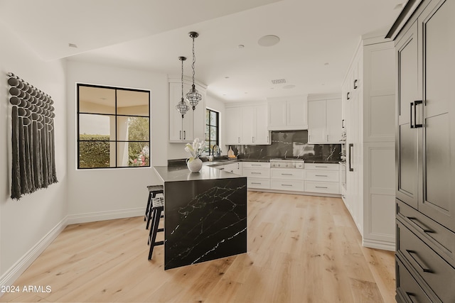 kitchen featuring a kitchen breakfast bar, light hardwood / wood-style flooring, pendant lighting, white cabinets, and decorative backsplash