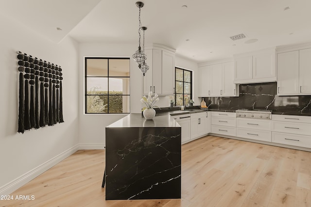 kitchen with white cabinets, light wood-type flooring, hanging light fixtures, and decorative backsplash