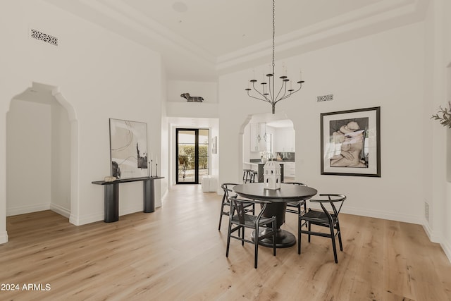 dining area with light hardwood / wood-style flooring, a towering ceiling, a notable chandelier, and a raised ceiling