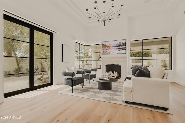 sitting room with a chandelier, a wealth of natural light, a towering ceiling, and light wood-type flooring