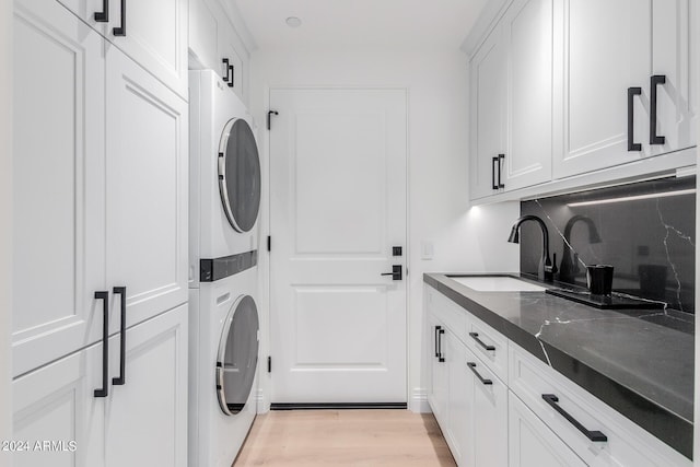 laundry area featuring cabinets, sink, light hardwood / wood-style flooring, and stacked washing maching and dryer