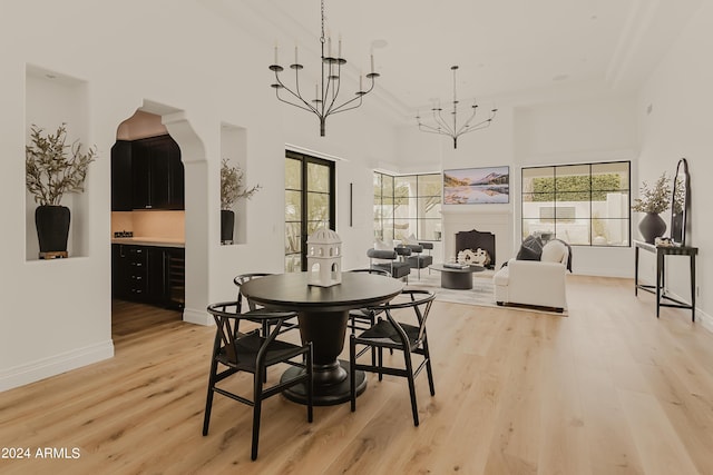 dining space featuring wine cooler, french doors, a high ceiling, light hardwood / wood-style floors, and an inviting chandelier