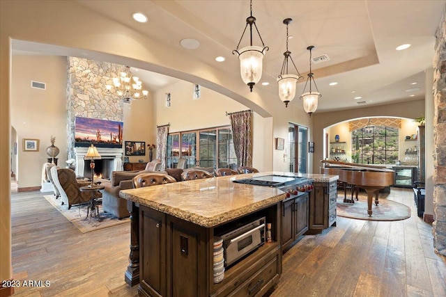 kitchen with light stone counters, dark brown cabinetry, hardwood / wood-style floors, and hanging light fixtures