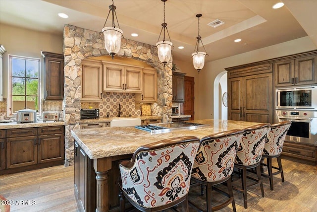 kitchen featuring light hardwood / wood-style flooring, backsplash, a large island, sink, and appliances with stainless steel finishes