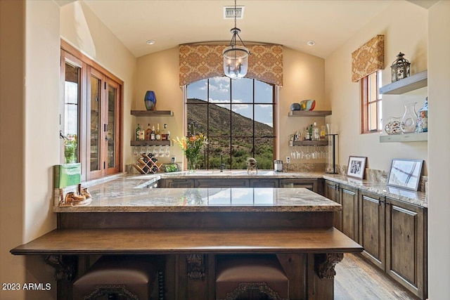 bar featuring light stone countertops, vaulted ceiling, dark brown cabinetry, and decorative light fixtures