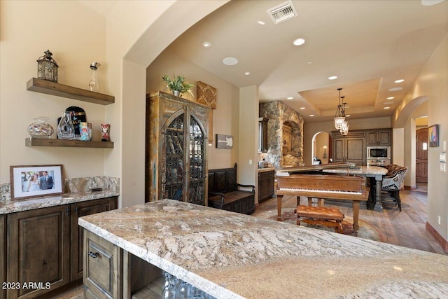 kitchen featuring hanging light fixtures, stainless steel microwave, a kitchen bar, dark wood-type flooring, and light stone counters