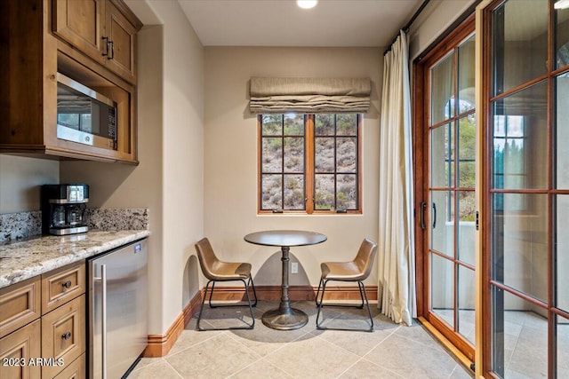 kitchen featuring wine cooler, light stone countertops, stainless steel microwave, and light tile patterned floors