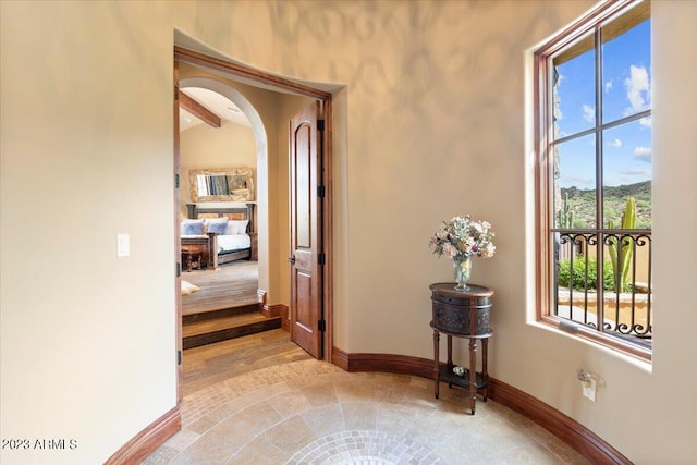 corridor with a healthy amount of sunlight, beamed ceiling, and light hardwood / wood-style flooring