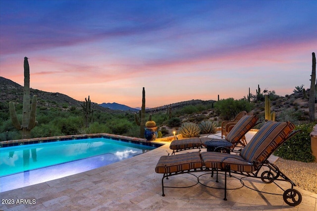 pool at dusk featuring a mountain view and a patio