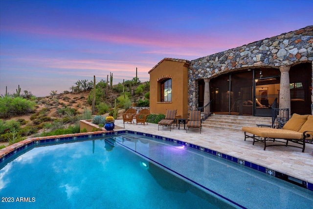 pool at dusk featuring a patio area and a sunroom