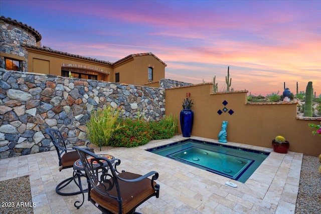 pool at dusk with a patio and an in ground hot tub