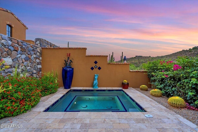 pool at dusk featuring an in ground hot tub