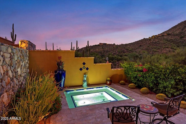 pool at dusk featuring a patio and an in ground hot tub