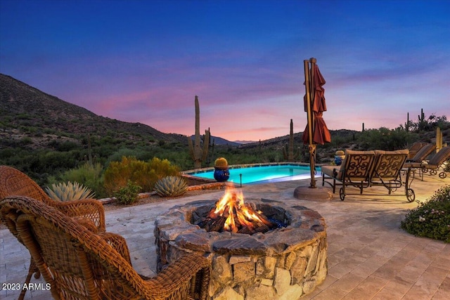 pool at dusk with a mountain view, a patio area, and a fire pit