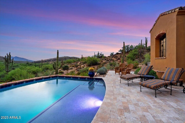 pool at dusk with a patio area and a mountain view