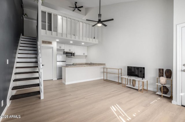 living room featuring ceiling fan, a towering ceiling, and light hardwood / wood-style flooring