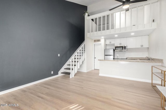 unfurnished living room featuring light hardwood / wood-style floors, ceiling fan, sink, and a towering ceiling