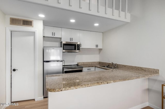 kitchen featuring kitchen peninsula, sink, light stone countertops, appliances with stainless steel finishes, and white cabinets