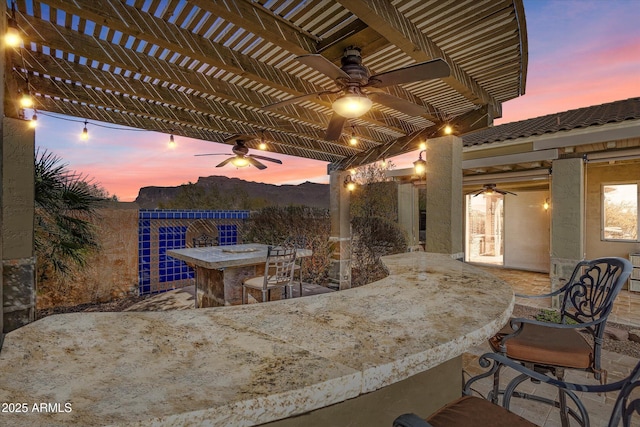 patio terrace at dusk with ceiling fan, exterior bar, and a pergola