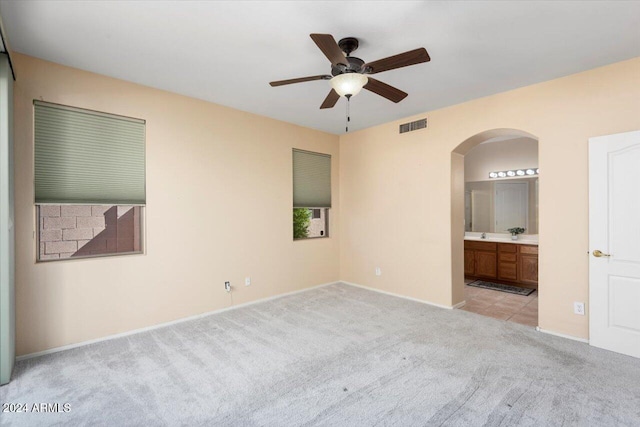 unfurnished bedroom with ensuite bath, light colored carpet, and ceiling fan