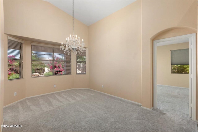 carpeted empty room with high vaulted ceiling and an inviting chandelier