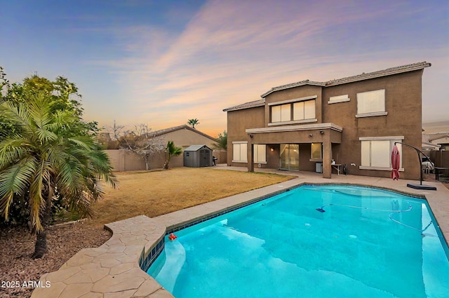 pool at dusk with a fenced in pool, a shed, an outdoor structure, a fenced backyard, and a patio